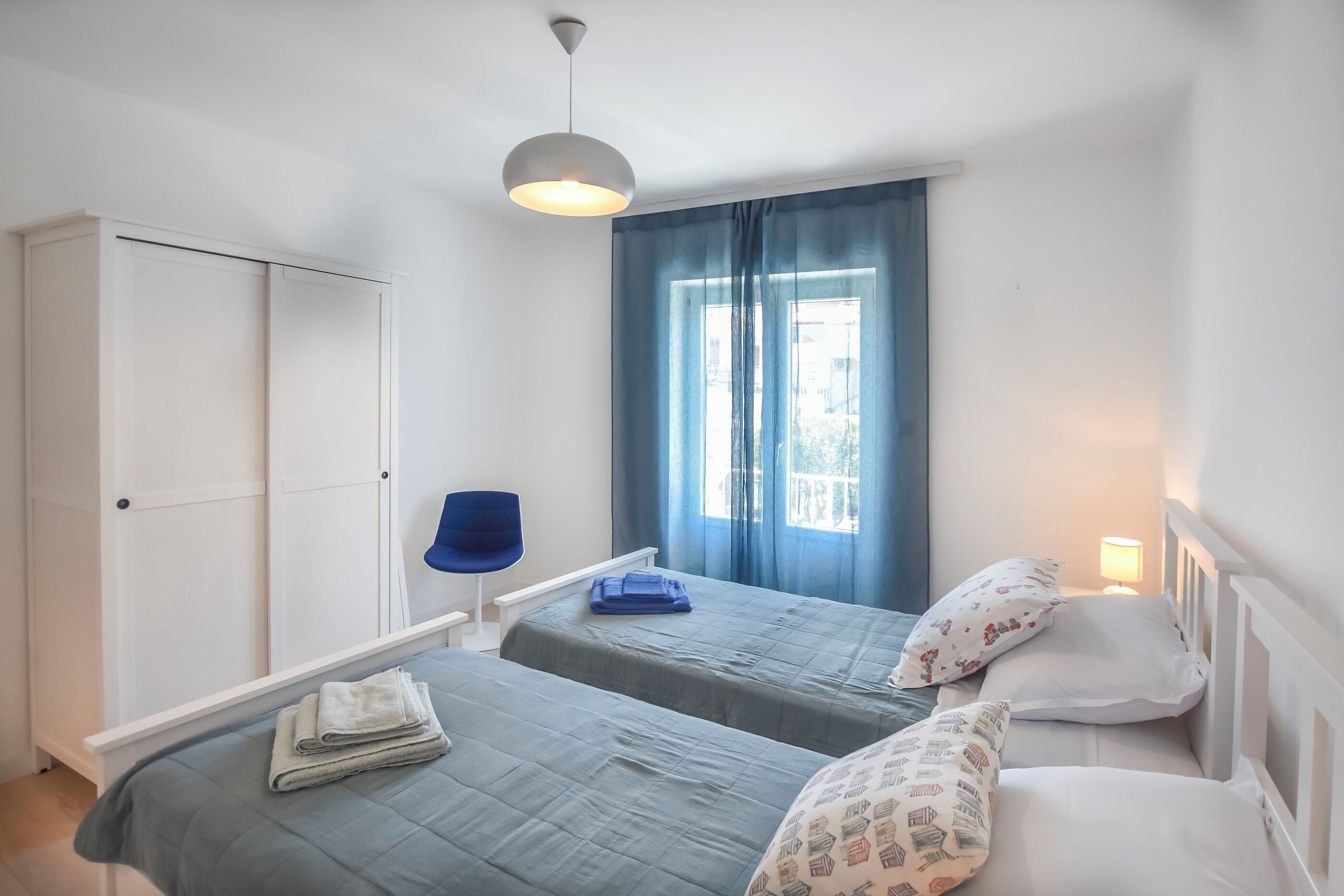 Een slaapkamer met twee bedden, een kledingkast, een stoel en een raam met gordijnen.