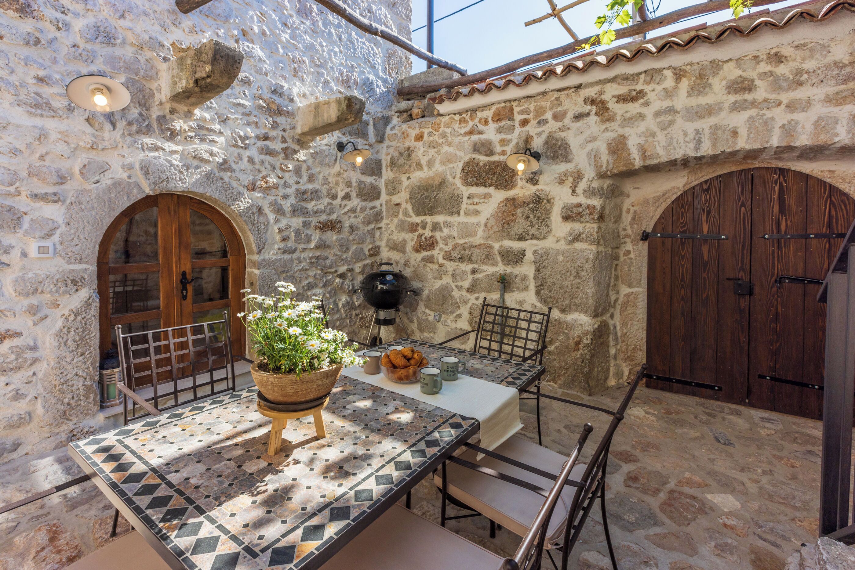 A stone-walled outdoor patio with a tiled table, chairs, and a potted plant.