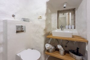Ein Badezimmer mit Toilette, Waschbecken auf einer Holzhilfe, einem Spiegel über dem Waschbecken und einem Handtuchhalter mit Handtüchern.