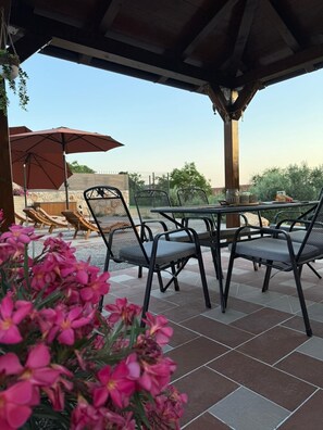 Eine Terrasse im Freien mit einem runden Tisch und Stühlen, umgeben von rosa Blüten.