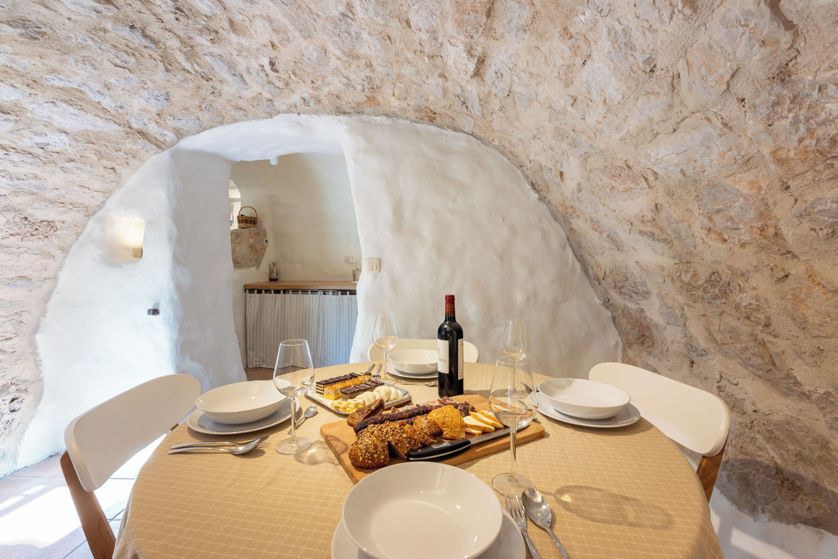 Una mesa de comedor dispuesta con platos, cubiertos y una botella de vino en una habitación con paredes de piedra y decoración rústica.