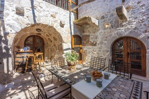 Un cortile con pareti in pietra, un tavolo piastrellato apparecchiato per mangiare, circondato da sedie e una botte di legno.