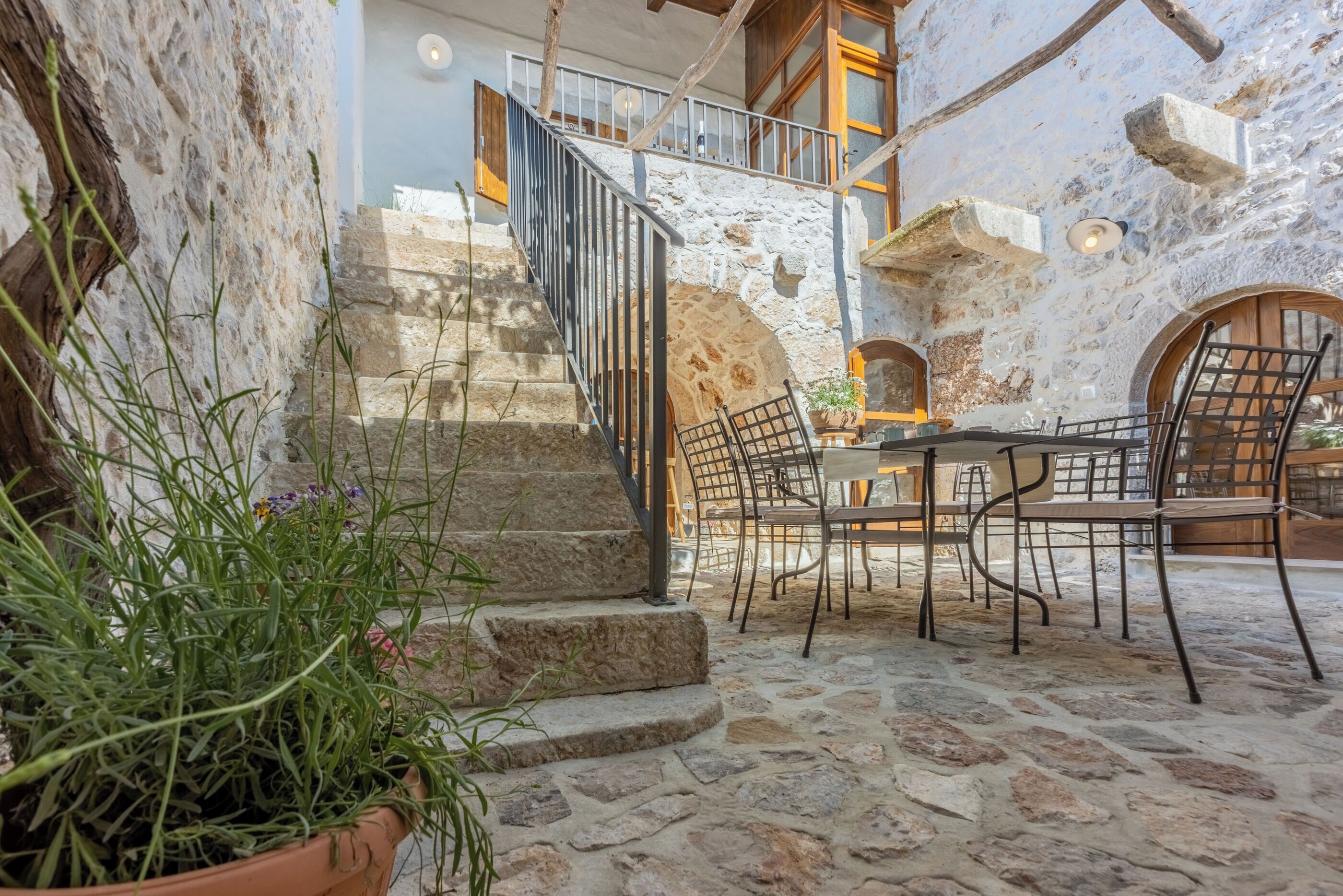 A stone courtyard with a staircase, outdoor seating, and a view of the interior.