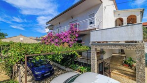 Ein zweistöckiges Haus mit Balkon, einem Auto auf der Einfahrt und einem Garten mit blühenden Pflanzen.