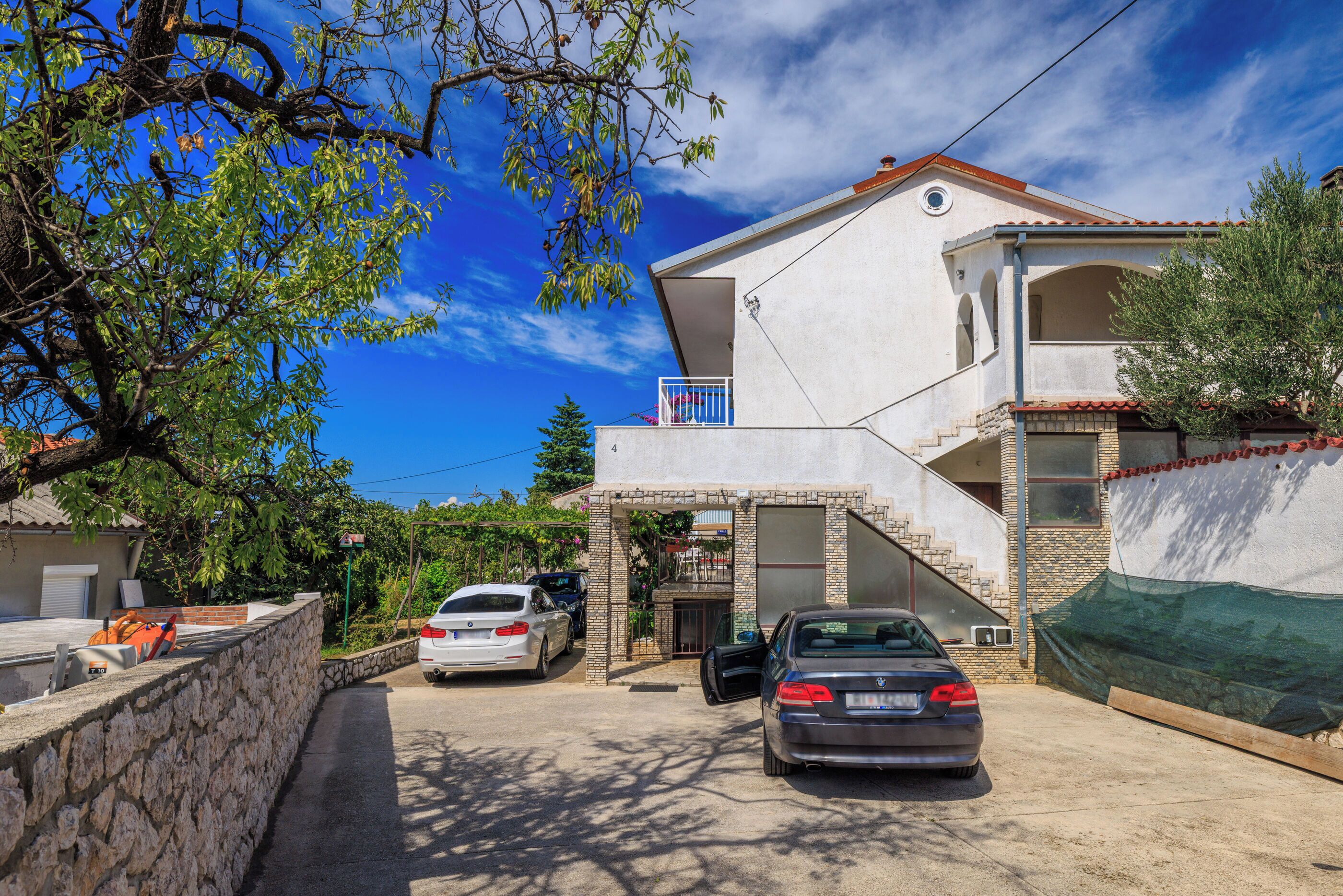 A two-story house with a balcony, a garage, and a driveway with two cars parked.