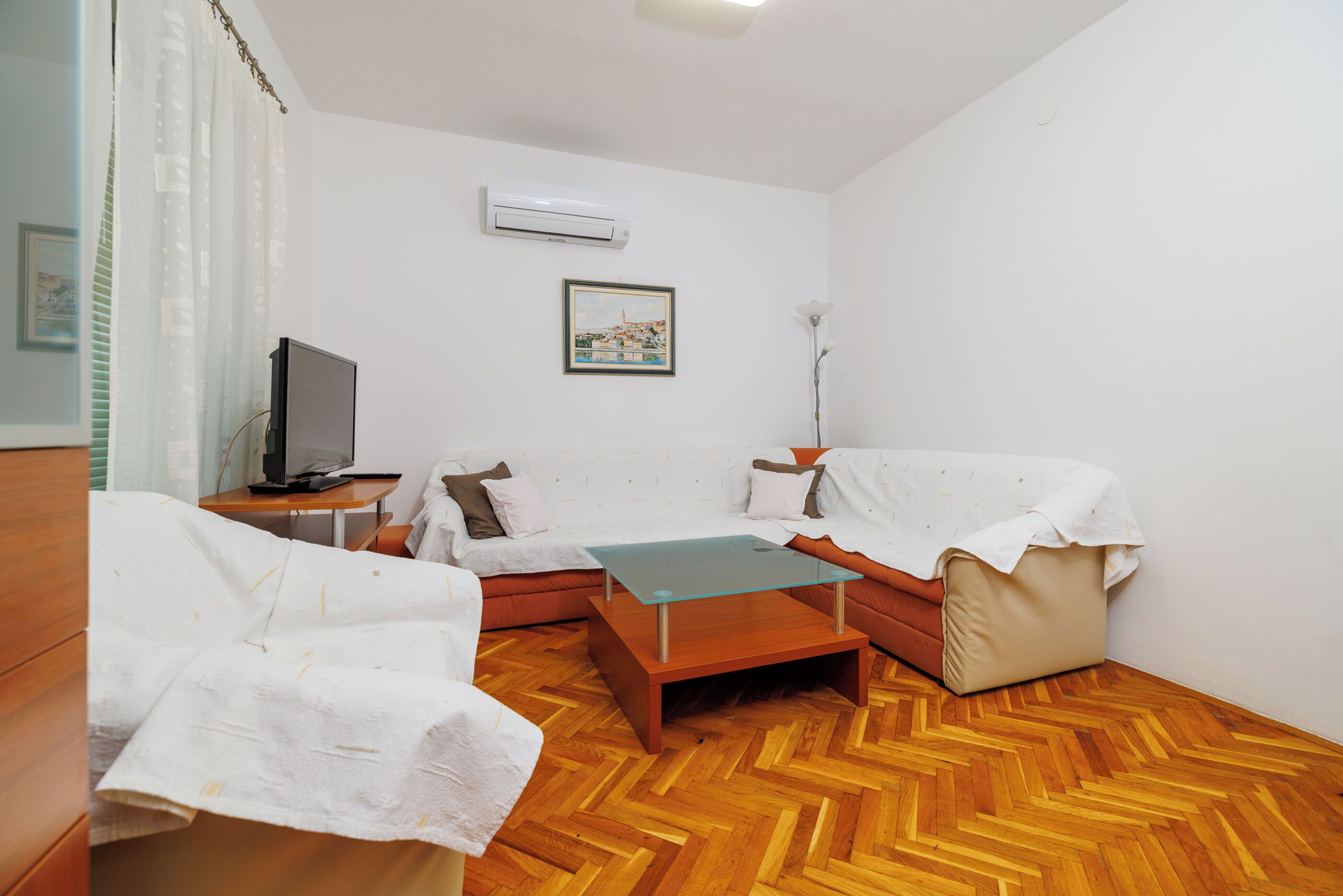 A modern living room with a sofa, a glass coffee table, a TV, and an air conditioning unit.