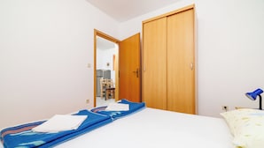 Ein Schlafzimmer mit einem Bett, einer blauen Decke, einem weißen Kopfkissen, einem Holzschrank und einer Schreibtischlampe.