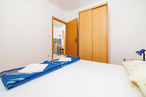 Una camera da letto con un letto, una coperta blu, un cuscino bianco, un armadio in legno e una lampada da scrivania.