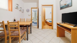 Ein kleiner Wohnbereich mit Essbereich, einem Bett, einem Fernseher und einem durch eine offene Tür einsehbaren Badezimmer.