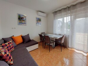A living room with a sofa, a dining table with chairs, and two wall-mounted air conditioning units. - Apartments Katica (Crikvenica)