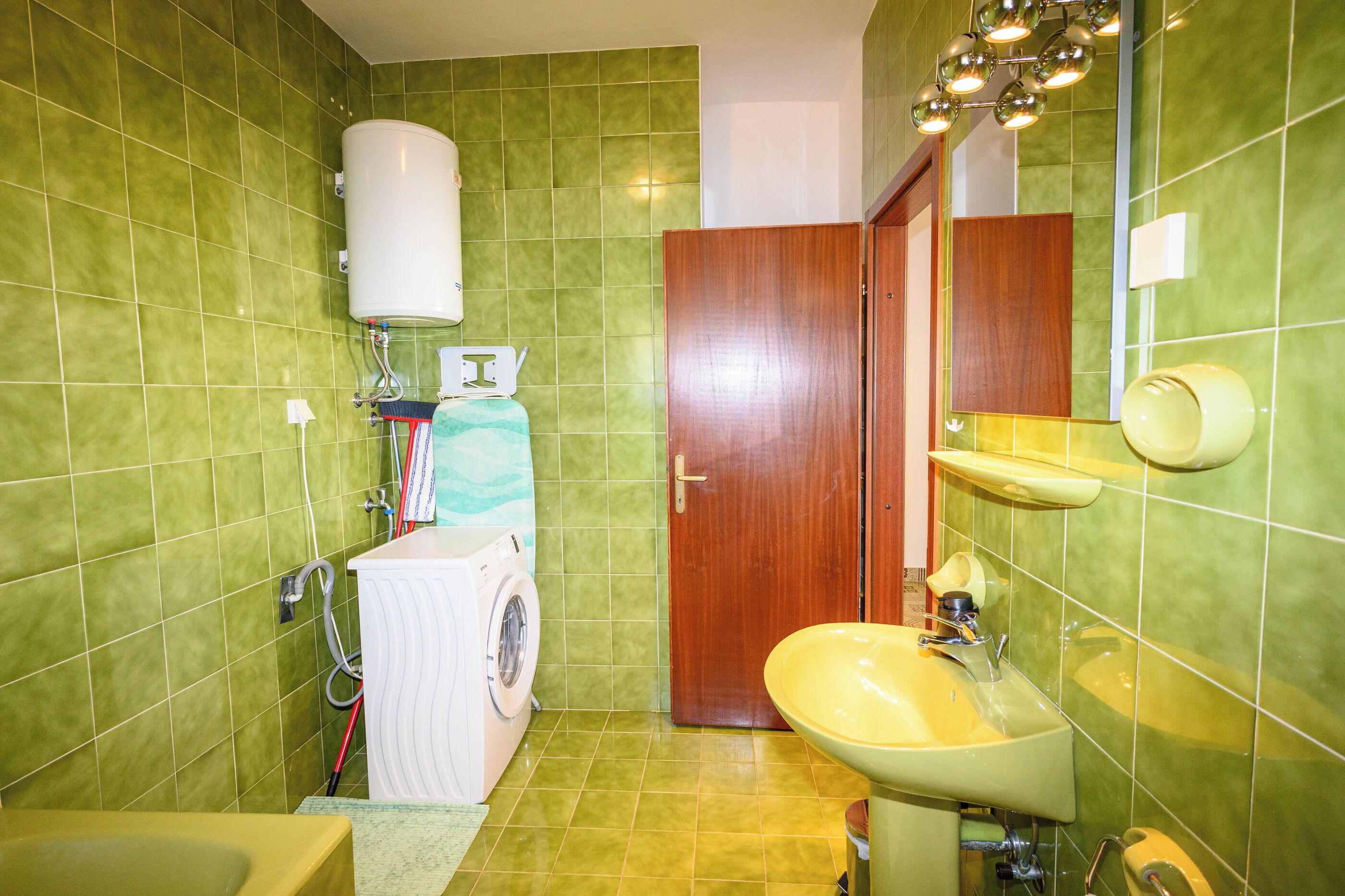 Ein Badezimmer mit grünen Fliesen, einer Waschmaschine, einem Waschbecken und einer Toilette.