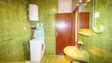 Ein Badezimmer mit grünen Fliesen, einer Waschmaschine, einem Waschbecken und einer Toilette.
