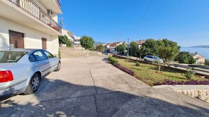 A residential street with a white car parked on the left, a stone pathway, and houses with balconies. - Apartments Vesna (Novi Vinodolski)