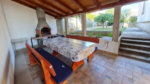An outdoor patio with a wooden table and benches, a brick oven, and a view of a garden. - Apartments Vesna (Novi Vinodolski)