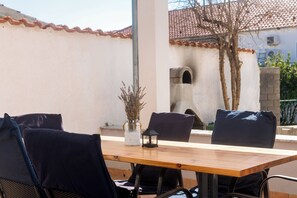 An outdoor dining area with a wooden table and black chairs, a vase with dried plants, and a stone wall with a small archway in the background. - Apartments Anita Tribunj (Tribunj)