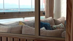 Una habitación con un ventanal grande con vistas al océano, un sofá con cojines y paneles de madera.