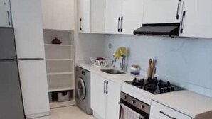 Une cuisine moderne avec des meubles blancs, un lave-linge encastré, une cuisinière et un évier.