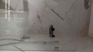 Une salle de bain dotée d’une douche à parois de verre, de murs en marbre et d’un robinet apparent.