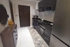 A modern kitchen with dark cabinetry, a stainless steel refrigerator, and a patterned rug. - Welcome home! (Kénitra)
