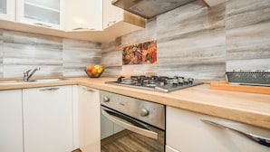 A modern kitchen with white cabinets, a gas stove, a sink, and a fruit bowl on the countertop. - Apartment Rota (Sveti Filip i Jakov)