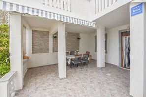 Un espace extérieur abrité, aménagé pour les repas, avec une table et des chaises, un balcon doté d’un auvent à rayures et une enseigne indiquant qu’il s’agit d’un appartement.