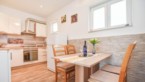 A modern kitchen with wooden cabinets, a built-in oven, and a dining area with a table and chairs. - Apartment Rota (Sveti Filip i Jakov)