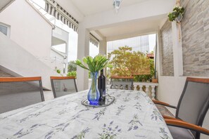Un coin repas avec une table dressée pour deux personnes, agrémenté d’une nappe à motifs floraux et d’un vase bleu contenant des plantes vertes.