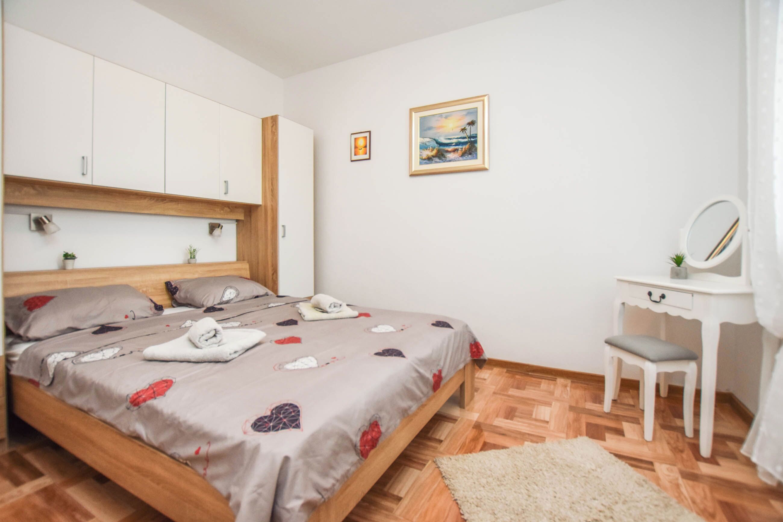 Une chambre avec un lit en bois, un bureau blanc avec un miroir et un tableau accroché au mur.