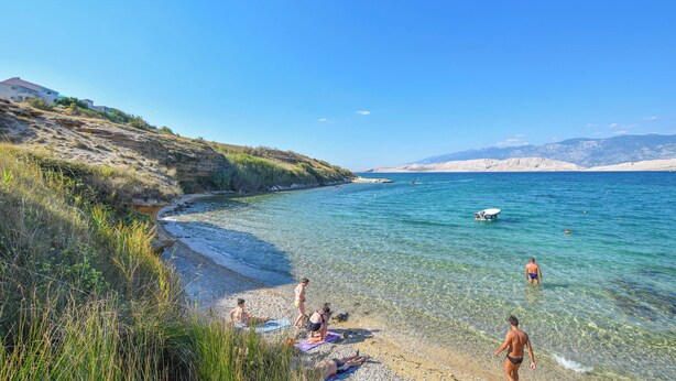 Ein Strand mit klarem Wasser, badenden Personen und einem Schiff in der Ferne.
