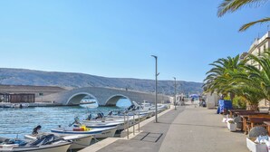 Ein Küstenhafen mit vertäuten Booten, einem Fußweg und einer Brücke im Hintergrund.