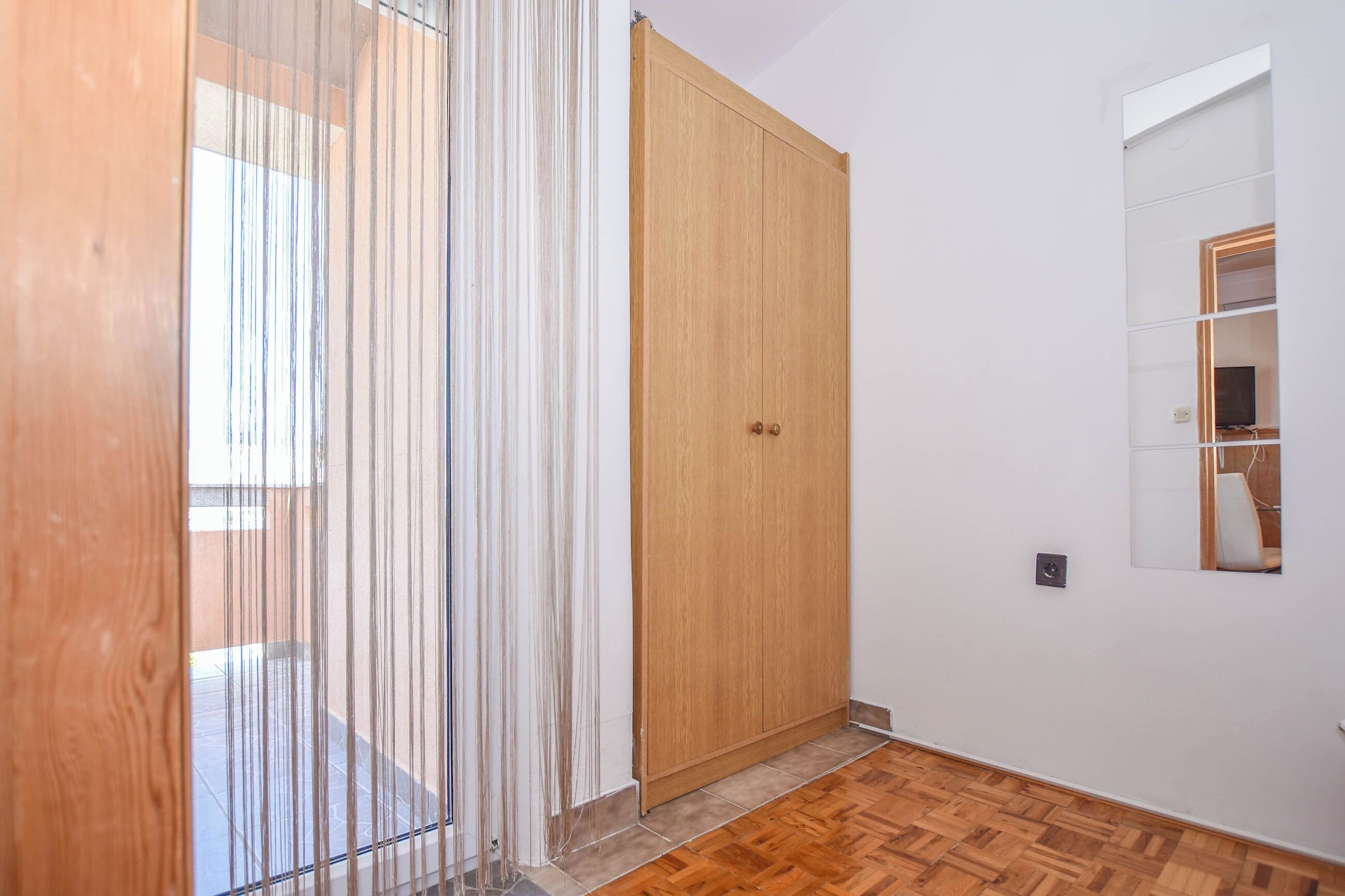 Un couloir avec un plancher en bois, une grande armoire en bois et un miroir au mur.