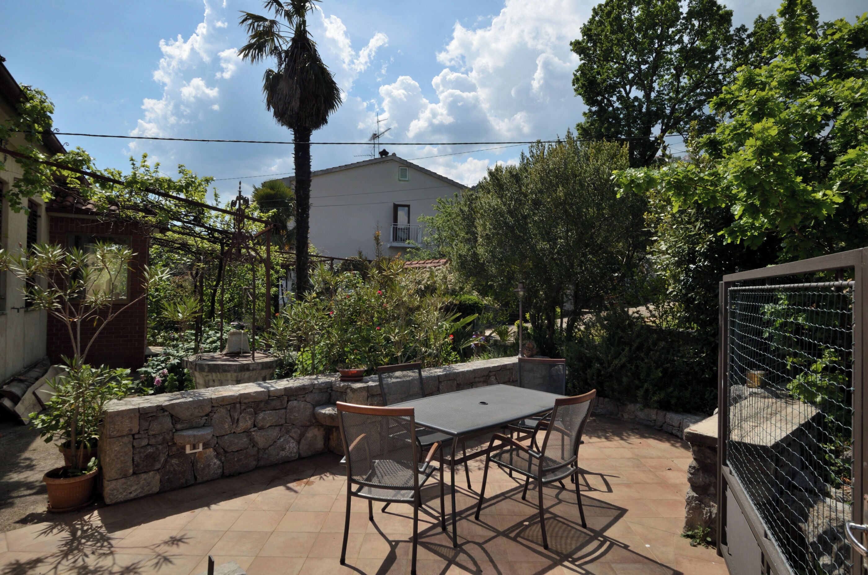 An outdoor patio with a table and chairs, surrounded by stone walls and potted plants.
