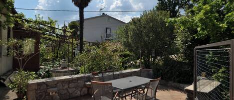 An outdoor patio with a table and chairs, surrounded by stone walls and potted plants.