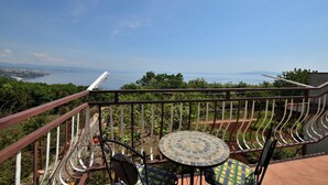 Ein Balkon mit Metallgeländer, einem runden Tisch mit Stühlen und Blick auf ein Gewässer und Grünflächen.