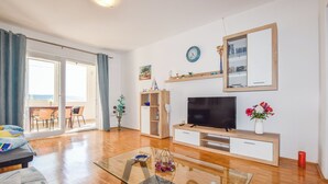 En moderne stue med et fladskærms-tv, træmøbler, et glasbord og en balkon med udsigt.