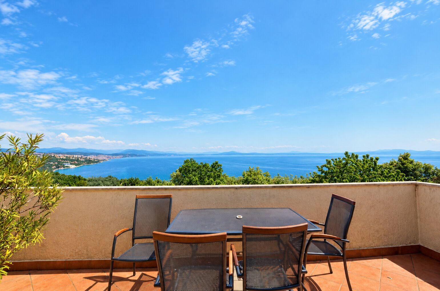 An outdoor patio with a table and chairs, overlooking a coastal landscape with a clear sky.