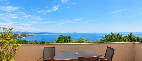 An outdoor patio with a table and chairs, overlooking a coastal landscape with a clear sky.