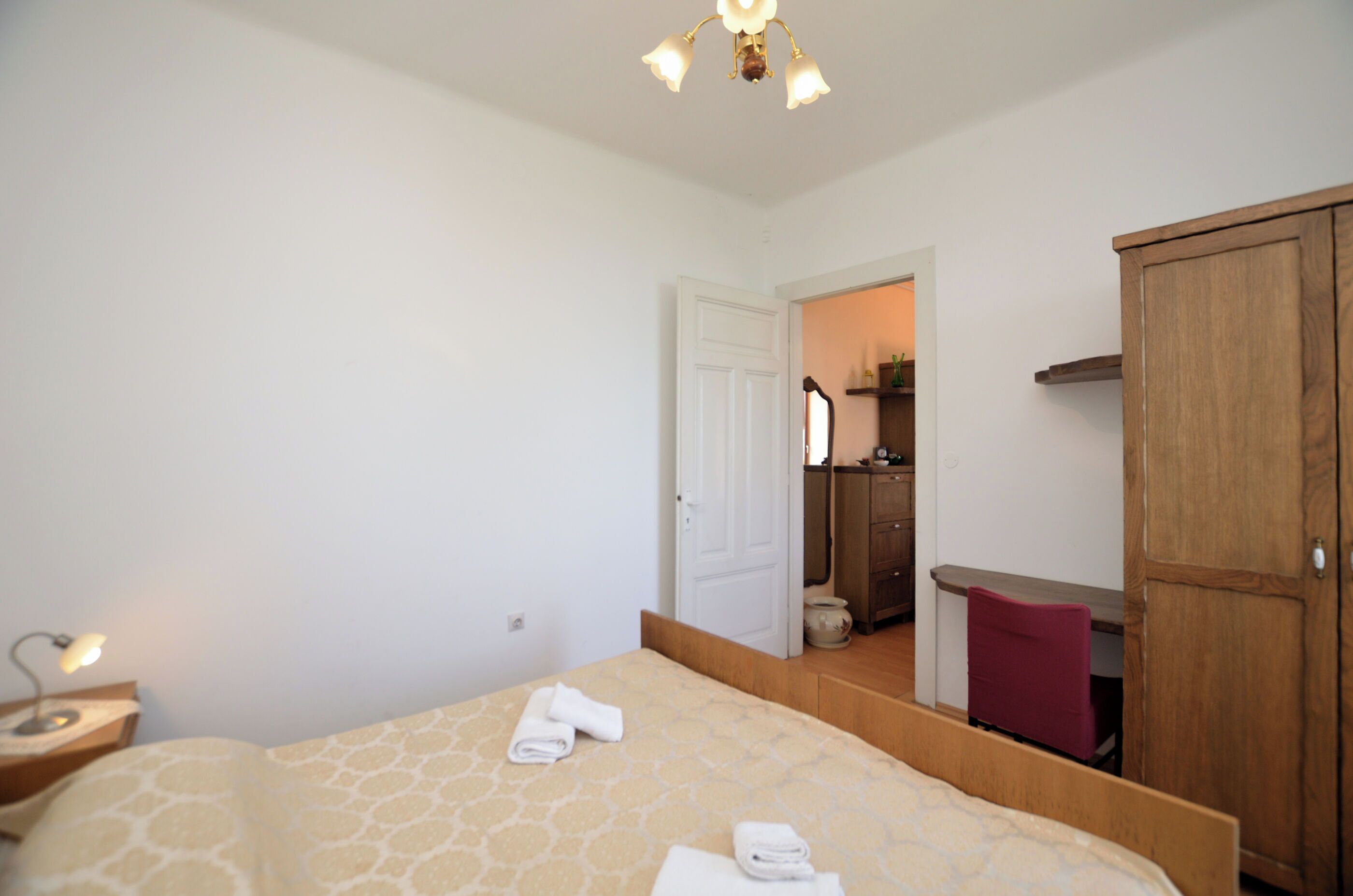 Una camera da letto con un letto, un comodino, una scrivania, un armadio e un bagno visibile attraverso una porta aperta.