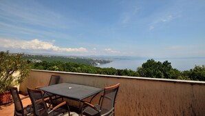 A terrace with a table and chairs overlooking a scenic view of a coastline and distant mountains. - Apartment Mirela (Opatija)