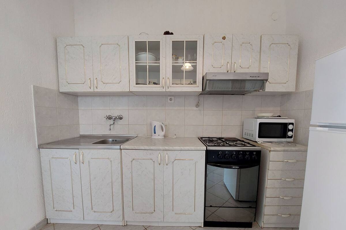 Une cuisine compacte avec des meubles blancs, une cuisinière à gaz, un four à micro-ondes et un lave-vaisselle.