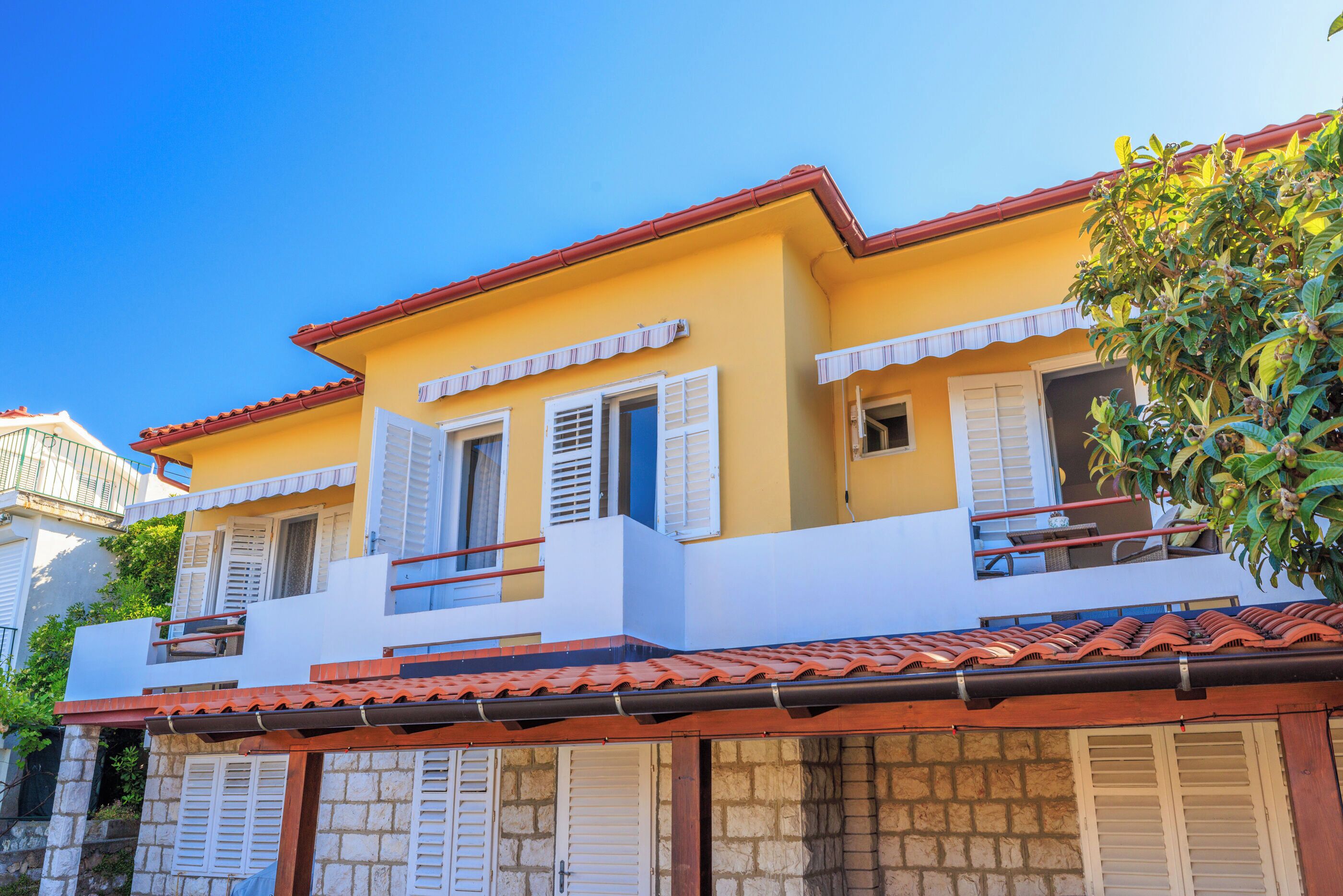 A two-story building with a yellow facade, white shutters, and a red-tiled roof.