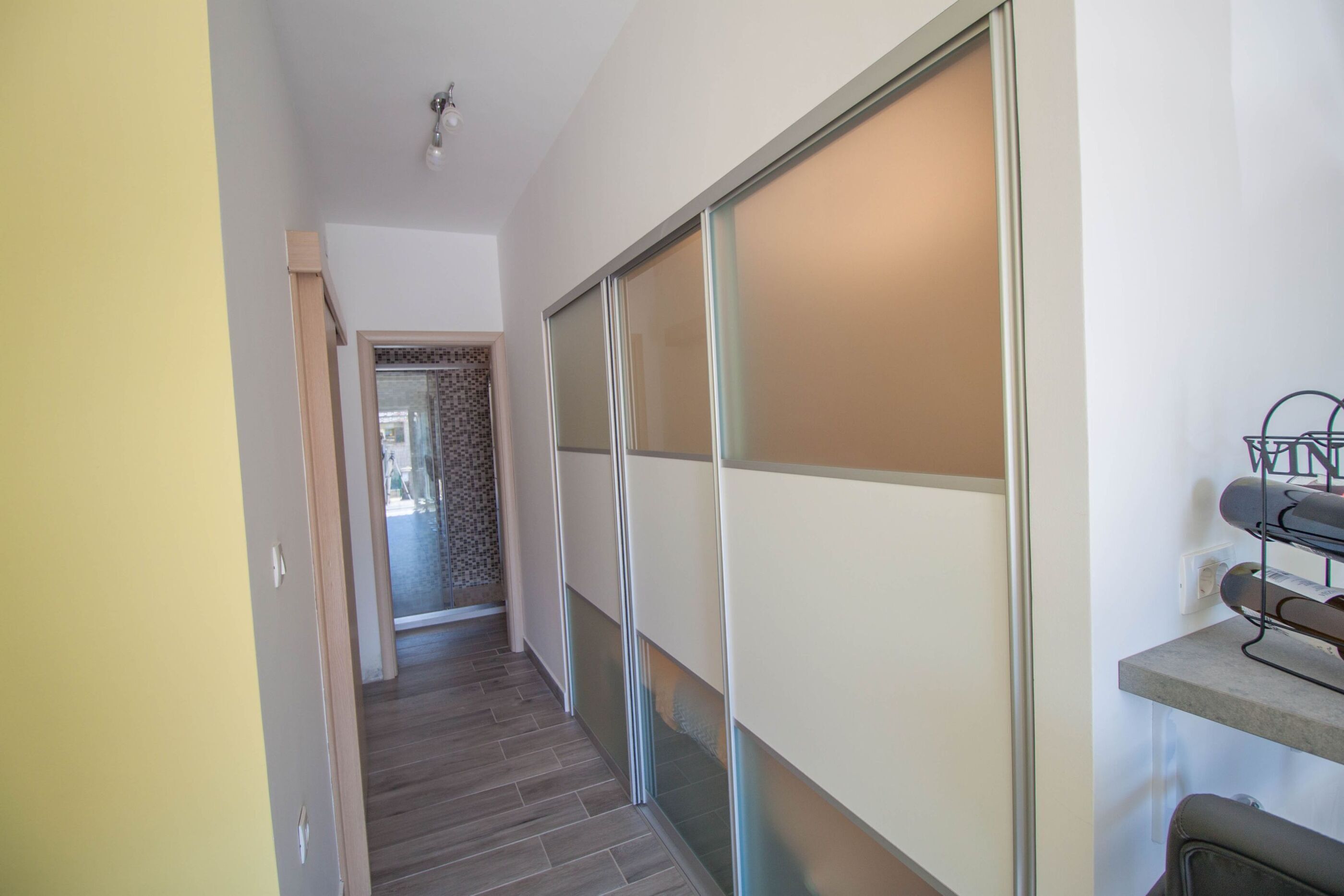 A hallway with a sliding door, a tiled floor, and a shoe rack on the right.
