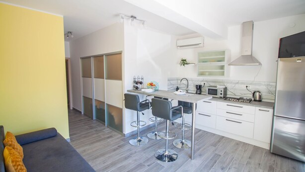 A modern kitchen with a dining area, white cabinets, and a grey sofa. - Apartment Smile (Opatija)