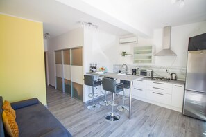 A modern kitchen with a dining area, white cabinets, and a grey sofa. - Apartment Smile (Opatija)