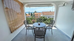 Varanda com mesa redonda, quatro cadeiras, um biombo de bambu e vista para prédios e árvores.