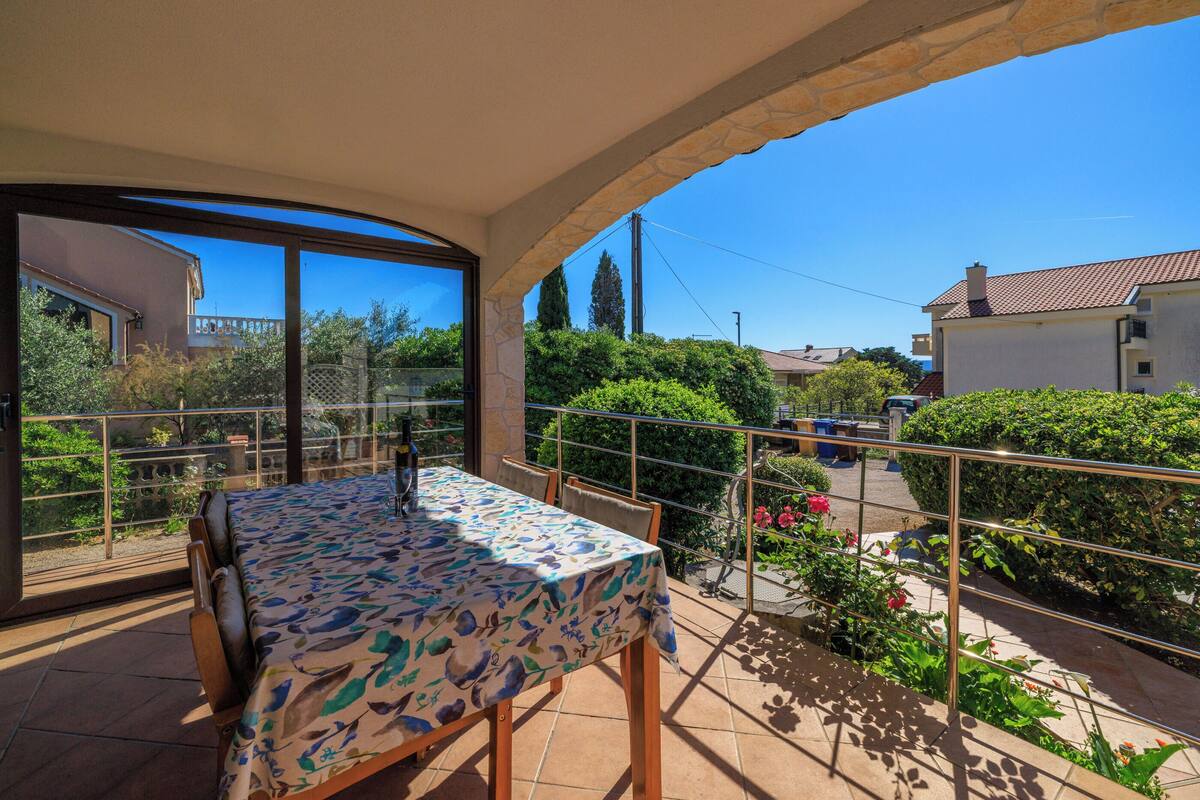 A balcony with a table and chairs, a view of the neighborhood, and a clear blue sky.