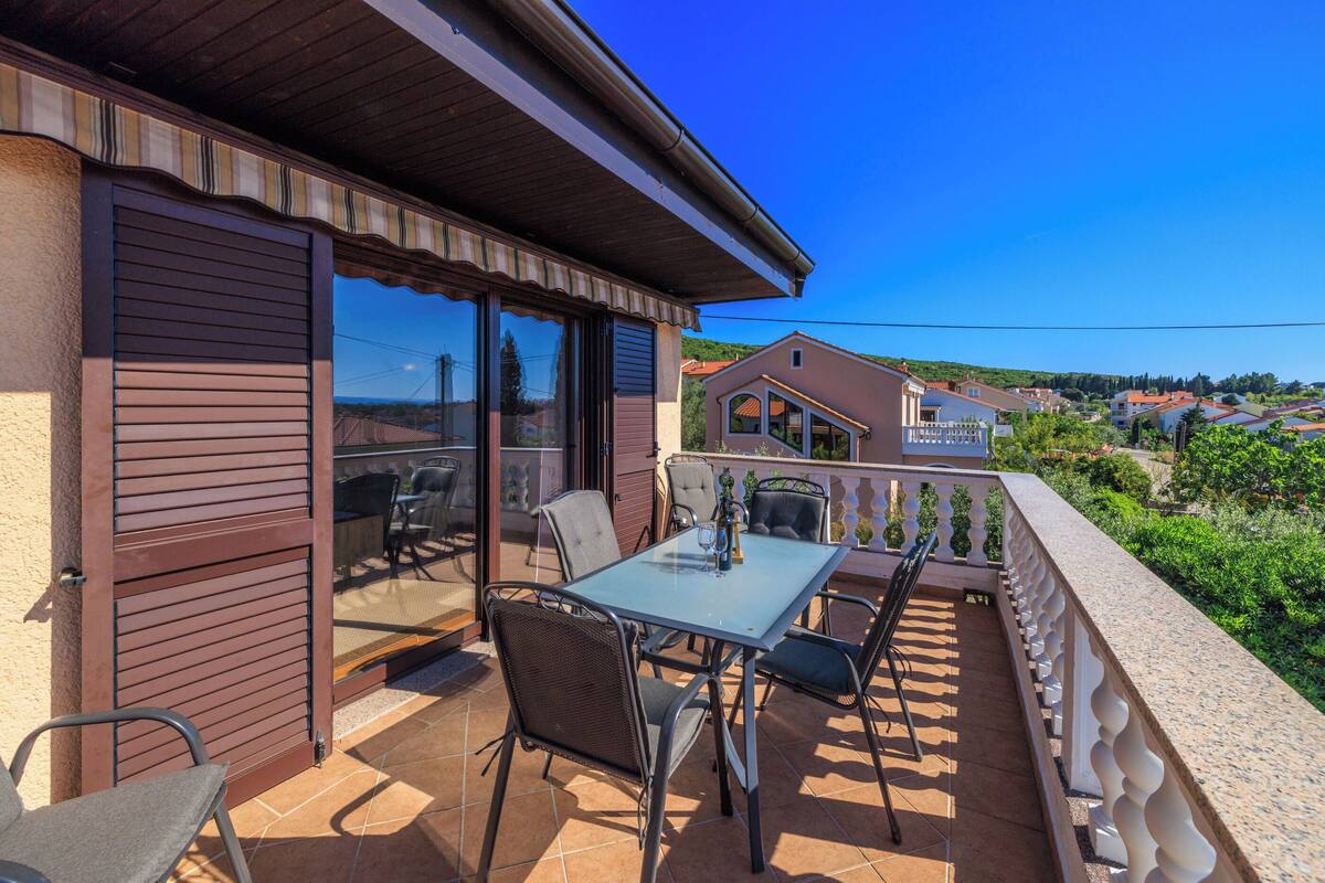 A patio with a table and chairs, a sliding glass door, and a view of the surrounding neighborhood.
