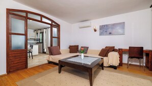 Een woonkamer met een houten salontafel, een beige bank en een eethoek met een houten tafel en stoelen.