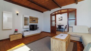 Een ruime woonkamer met houten vloeren, een witte bank, een houten salontafel en een televisie op een witte kast.