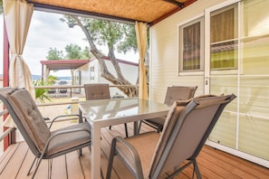 A covered outdoor dining area with a table and chairs, a view of a house, and a tree. - Mobile Home Dandelion (Biograd na Moru)